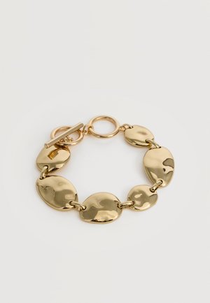 Bracelet épais ton or avec des maillons ovales irréguliers grands et petits alternés et un fermoir toggle sur fond blanc.