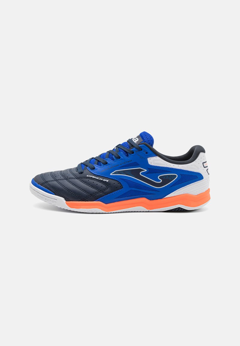 Zapatilla deportiva azul y negra con diseño texturizado, lengüeta acolchada, acento naranja en la suela y detalles en blanco. Presenta cierre con cordones.