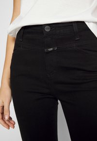 Jeans de denim negro con un diseño ajustado, que presentan un cierre de botón, cinco bolsillos y detalles de costura sutiles.