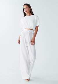 Biały, prążkowany dwuczęściowy zestaw składający się z krótkiego topu z krótkimi rękawami oraz luźnych spodni z elastycznym pasem i sznurkiem do regulacji.