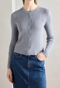 Šedý žebrovaný kardigan s knoflíkovým zapínáním, kulatým výstřihem a dlouhými rukávy, doplněný tmavou džínovou sukní. Hladká textura.