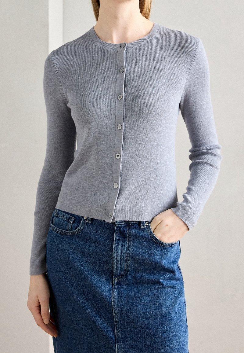 Šedý žebrovaný kardigan s knoflíkovým zapínáním, kulatým výstřihem a dlouhými rukávy, doplněný tmavou džínovou sukní. Hladká textura.