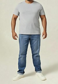 Hellgraues T-Shirt mit kurzen Ärmeln, blaue Jeans und weiße Slip-On-Schuhe. Der Schnitt ist leger, mit rundem Ausschnitt und entspannter Silhouette.