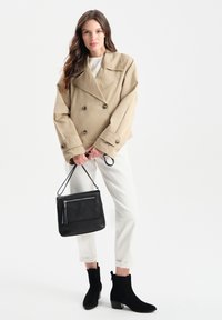 Beżowa marynarka na podwójne zapięcie, czarna torba na ramię z frędzlami, białe spodnie oraz czarne zamszowe botki za kostkę na słupku.