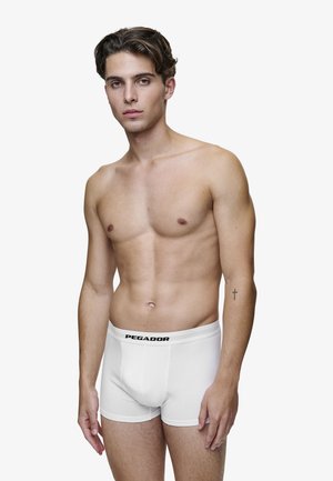 Weiße Baumwoll-Boxershorts mit einem schwarzen "PEGADOR"-Bund, die eine figurbetonte Passform und eine glatte Textur bieten. Modell trägt sie.