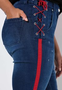 Tummansiniset farkut, joissa on edessä nauhakiinnitys punaisella nauhalla, sivussa punainen raita ja klassinen takatasku. Hieman kuluneita yksityiskohtia.