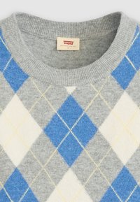 Pull en tricot gris avec un motif argyle bleu et blanc, rehaussé de accents jaunes et d'un col côtelé. Étiquette de la marque visible au niveau du col.