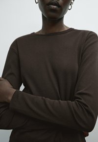 Brown long-sleeve shirt made of soft fabric. Simple round neckline, fitted sleeves, and smooth texture, with a minimal design.