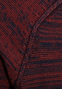 Tessuto testurizzato in rosso scuro e blu navy con un motivo intrecciato, caratterizzato da una cucitura visibile e una finitura liscia e morbida.