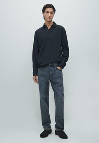 Dunkles, langärmliges Poloshirt mit Kragen, kombiniert mit ausgewaschenen blauen Jeans. Schwarze Schuhe runden den lässigen Look ab. Minimalistisches Design und lockere Passform.