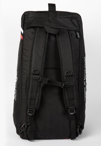 Black backpack with padded shoulder straps, top handle, and adjustable side straps. Features a white logo on one side and red accent.
