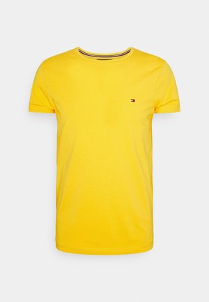T-shirt jaune à manches courtes avec col rond et petit logo Tommy Hilfiger sur la poitrine gauche sur fond blanc uni.