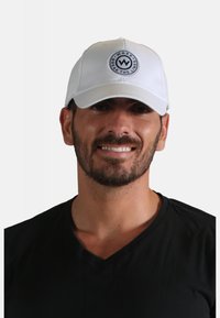 Casquette de baseball blanche avec un logo rond au centre, comportant les mots "WAXX" et "BREAK THE LINES". Tissu lisse, forme structurée.