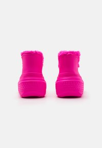 Stivali di gomma rosa brillante con un bordo soffice in cima; la suola testurizzata presenta piccoli punti rialzati per la presa. Design liscio e senza cuciture.