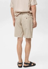 Beige gestreepte shorts van lichtgewicht stof met een achterzak en knoopdetail, gecombineerd met zwarte sandalen.