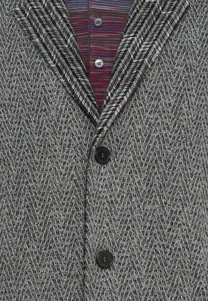 Grijze textuur blazer met een visgraatpatroon, zwarte knopen en een contrasterende gestreepte stof in de kraag en de binnenvoering.