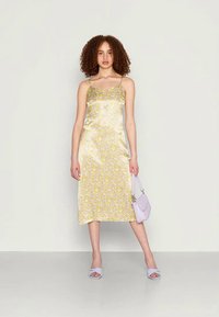 Vestido slip amarelo e branco com estampa floral, alças finas, acabamento em cetim, até ao joelho. Combinado com uma bolsa lavanda e sapatos a condizer.
