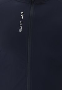 Marineblaue Radjacke aus glattem, dehnbarem Stoff. Verfügt über einen Reißverschluss vorne, reflektierende Akzente und den Schriftzug "ELITE LAB" an der Seite.