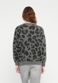 Grå strikkegenser med svart leopardmønster, med en fluffy tekstur og ribbede mansjetter, brukt sammen med grå jeans.