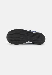 Suela de goma negra con patrón de agarre texturizado, con media suela blanca y acentos azules en la parte superior. Diseño simple y funcional.