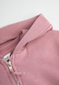 Różowa bluza z kapturem na zamek, wykonana z miękkiego materiału, z teksturowanym kapturem, zapięciem na zamek i akcentem w postaci sznurka. Gładkie wykończenie i luźny krój.