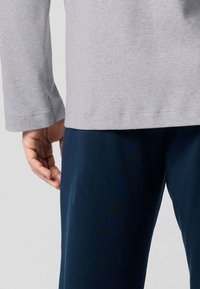 Maglietta grigia a maniche lunghe con una texture liscia, abbinata a pantaloni blu scuro, che mostrano una vestibilità rilassata e un design semplice.