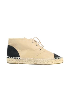 Chaussure à lacets en cuir beige avec tissu noir au talon et à l’orteil, dotée d’une semelle en jute tissée pour un usage décontracté.
