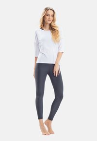 Witte top met driekwartmouwen in combinatie met strakke donkergrijze leggings, beide gemaakt van gladde, rekbare stof.