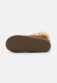 Brown suede slipper with a soft, fluffy cream lining, textured rubber sole, and subtle leopard print accents on the inside.