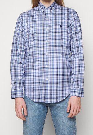 Man wearing blue and white checkered button-down shirt with long sleeves, paired with light blue jeans, torso visible.