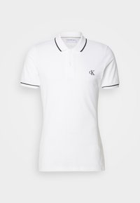 Polo blanc à manches courtes avec bordure noire sur le col et les manches, patte à deux boutons, et petit logo noir "cK" sur la poitrine gauche.