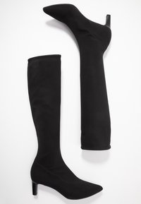 Bottes montantes en tissu noir avec bouts pointus et talon fin superposé. Texture lisse et design ajusté, avec matériau élastique pour le confort.