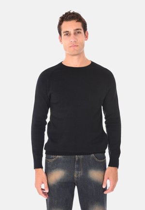 Maglione nero lavorato a maglia con collo rotondo, polsini e orlo a costine. Abbinato a jeans blu sbiaditi, che mettono in mostra un look casual e testurizzato.