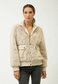 Creme faux fur og glat beige tekstiljakke. Har en lynlåslukning foran, to forlommer og gatherede ærmer.
