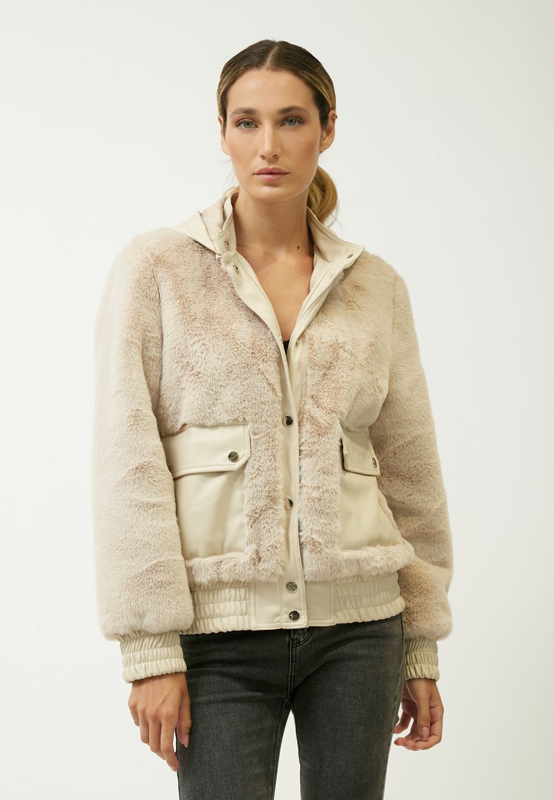 Creme faux fur og glat beige tekstiljakke. Har en lynlåslukning foran, to forlommer og gatherede ærmer.