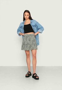 Saia cinza claro com um padrão de bolinhas, combinada com um top cropped preto e uma jaqueta de denim azul oversized; modelo a usar sandálias pretas de plataforma.