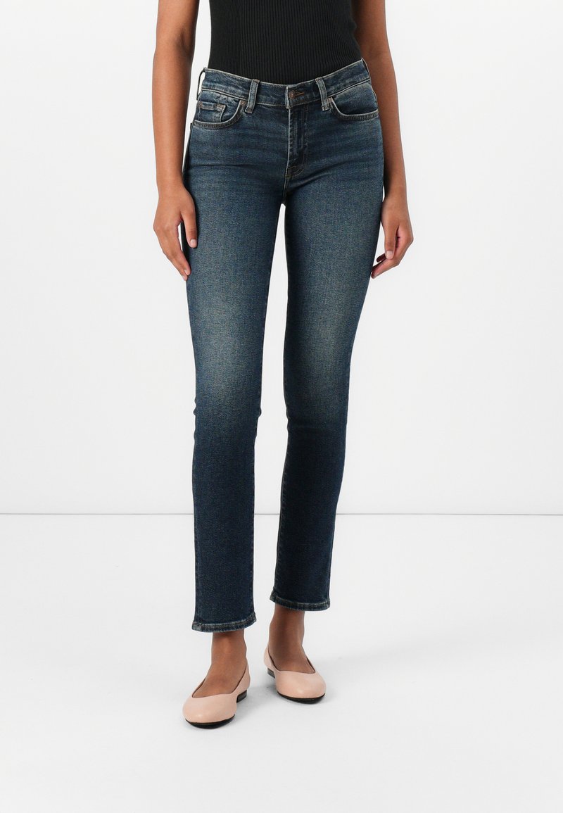 Donkerblauwe denim jeans met een slim fit, middelhoge taille, vijf-pocket ontwerp, en subtiele vervaging op de dijen, in combinatie met lichtroze ballerina's.