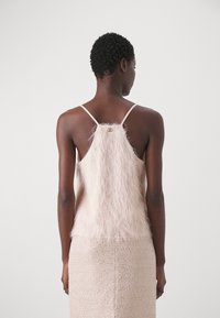 Top senza schienale di un tenue rosa chiaro e soffice con spalline sottili, abbinato a una gonna aderente e strutturata. Il top presenta un delicato dettaglio in metallo sul retro.