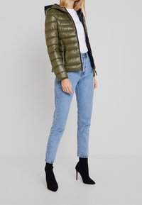 Olivgrön pufferjacka med huva, med dragkedjestängning och sidofickor. Kombinerad med ljusblå jeans och svarta klackstövlar.