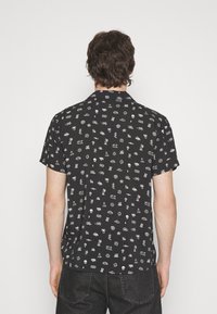 Maglietta nera a maniche corte con un motivo grafico bianco ripetuto che presenta vari simboli e forme sul retro. Materiale in cotone.