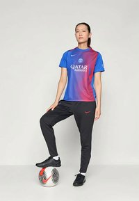 Mėlynai raudonas gradientinis sportinis marškinėliai su Qatar Airways logotipu, juodos sportinės kelnės ir juodi futbolo batai, stovintis ant raštuoto futbolo.