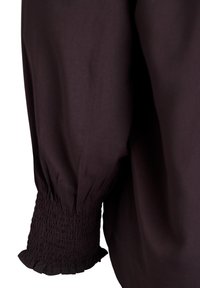 Mørk lilla bluse med rynket manchet, der har samlet stof og en blød tekstur, hvilket fremhæver en afslappet pasform og et flydende design.