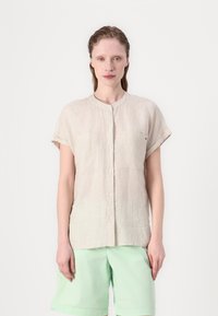 Camicia button-up a maniche corte a righe beige con colletto rotondo e due tasche sul petto, abbinata a pantaloni corti verde menta.