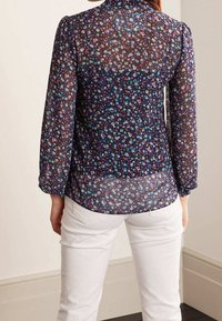 Blusa trasparente a maniche lunghe di colore blu navy con stampa floreale in rosa, verde e bianco; presenta un collo rotondo e polsini con bottoni.