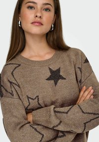 Brązowy sweter robiony na drutach z wzorem gwiazdy w ciemnym brązie, okrągły dekolt i ściągacze. Miękka faktura z luźnym krojem.