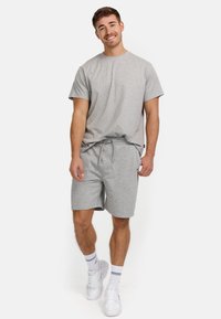 Grå bomulds t-shirt og matchende shorts med snor i livet. Hvide sneakers og ankelstrømper med en blå stribe synlig.