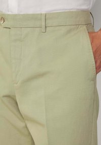 Hellgrüne Hosen aus einem weichen, glatten Stoff. Sie haben einen flachen Bund, seitliche Taschen und einen Knopfverschluss am Bund.