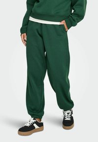 Grønne bomulds sweatpants med løstsiddende pasform, sidelommer og ribbet manchetter, brugt sammen med sorte sneakers med hvide detaljer.