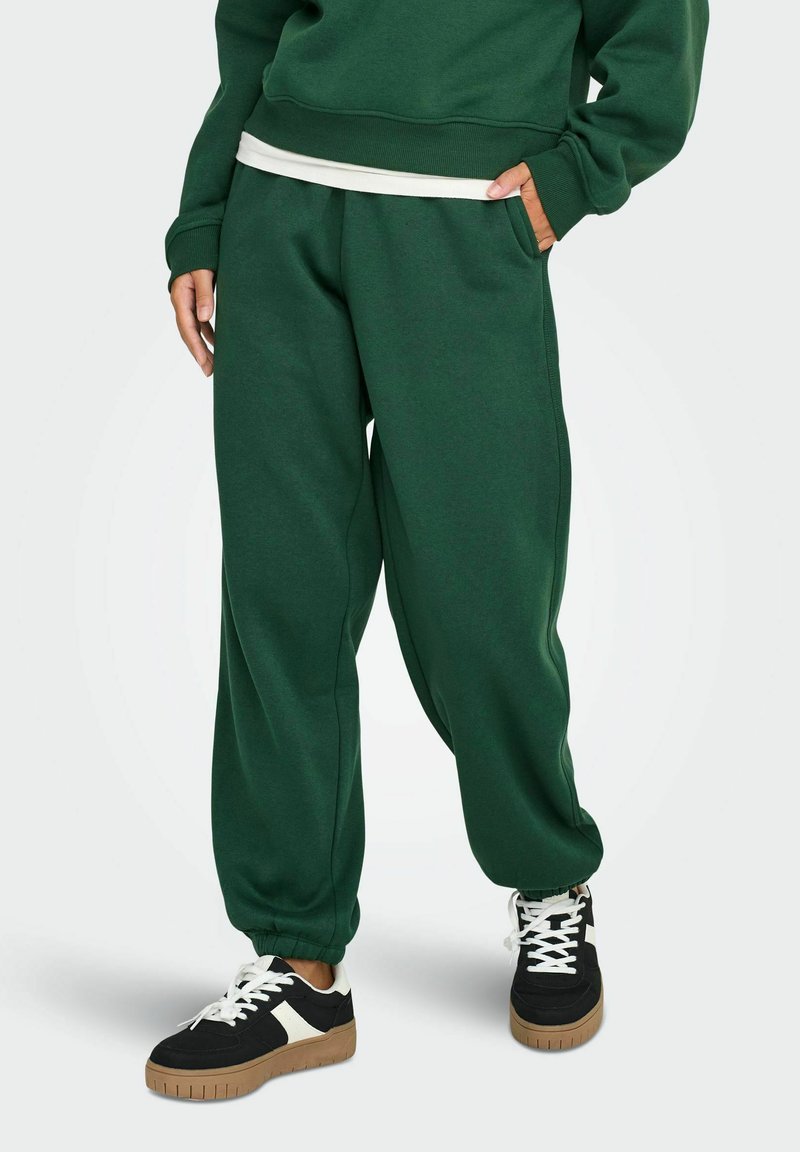 Grønne bomulds sweatpants med løstsiddende pasform, sidelommer og ribbet manchetter, brugt sammen med sorte sneakers med hvide detaljer.