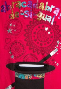 Röd t-shirt med flerfärgad glittrande text "abracadabra de si-gual," grafisk svart hatt med dekorativt band, omgiven av stjärnor och cirkulära mönster.